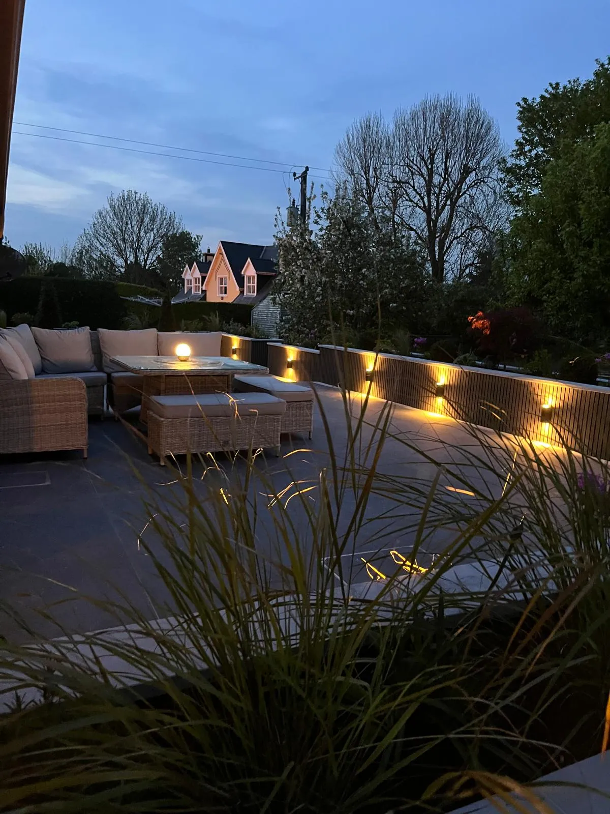 Outdoor lounge seating on a dark paved patio with built-in lighting at dusk
