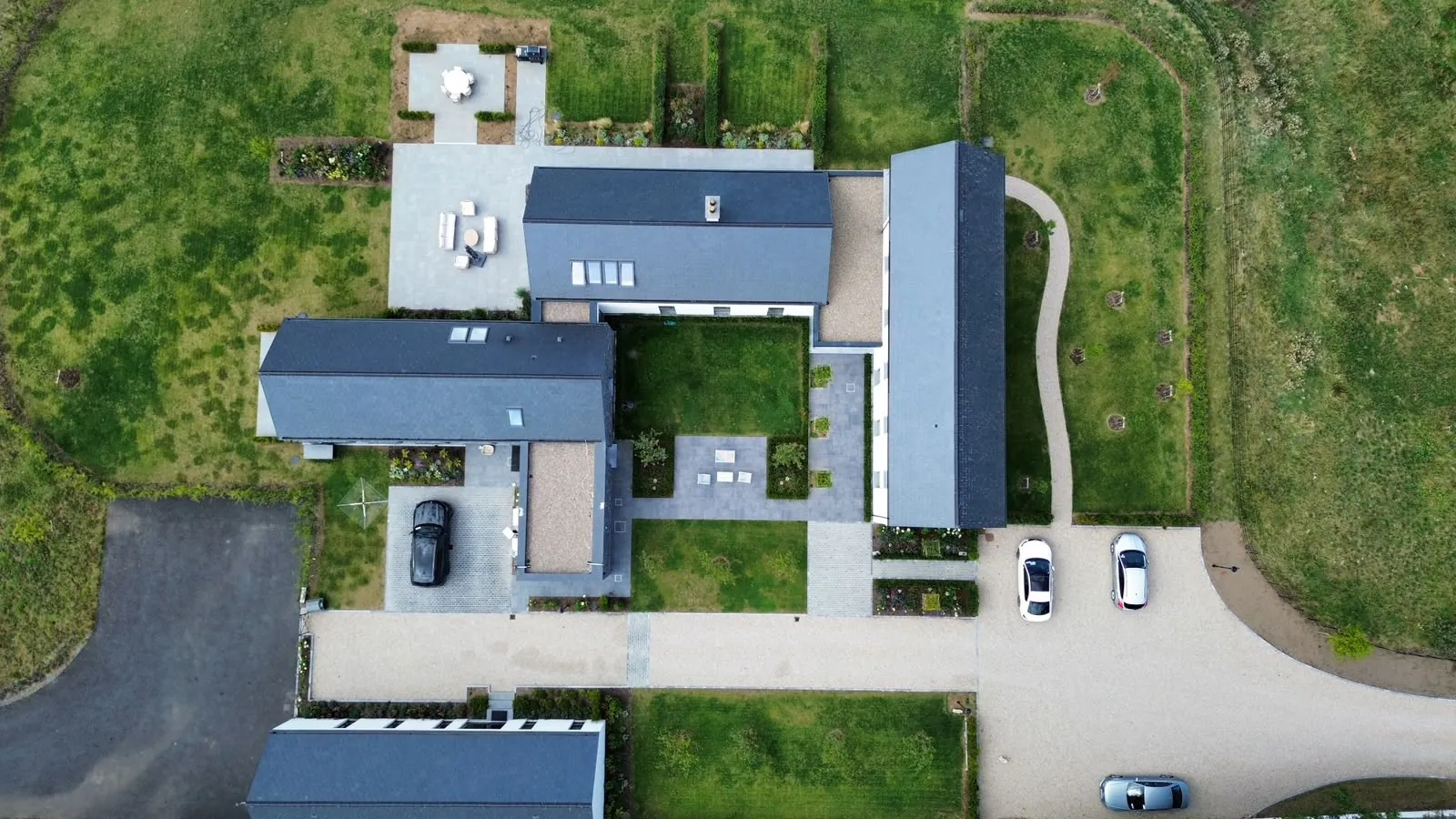Aerial view of a property with a paved driveway and gravel parking area