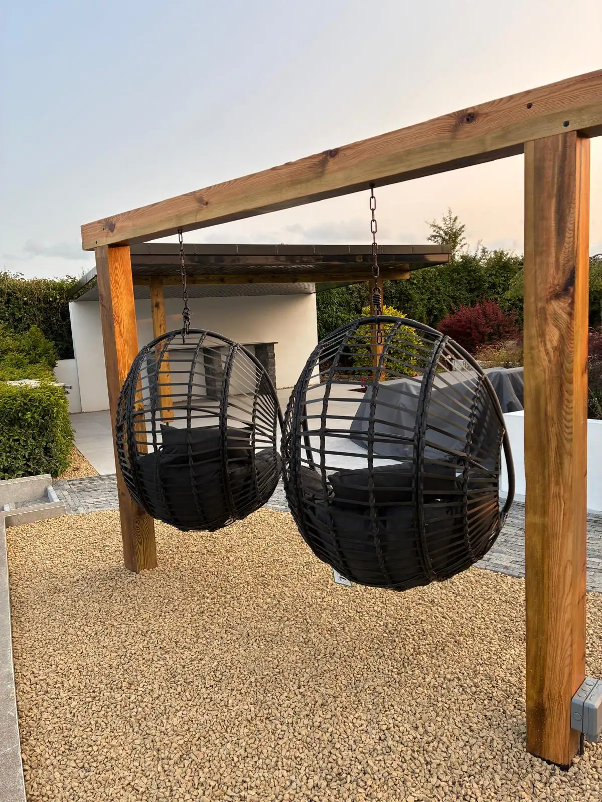 Timber pergola with hanging egg chairs over a gravel seating area