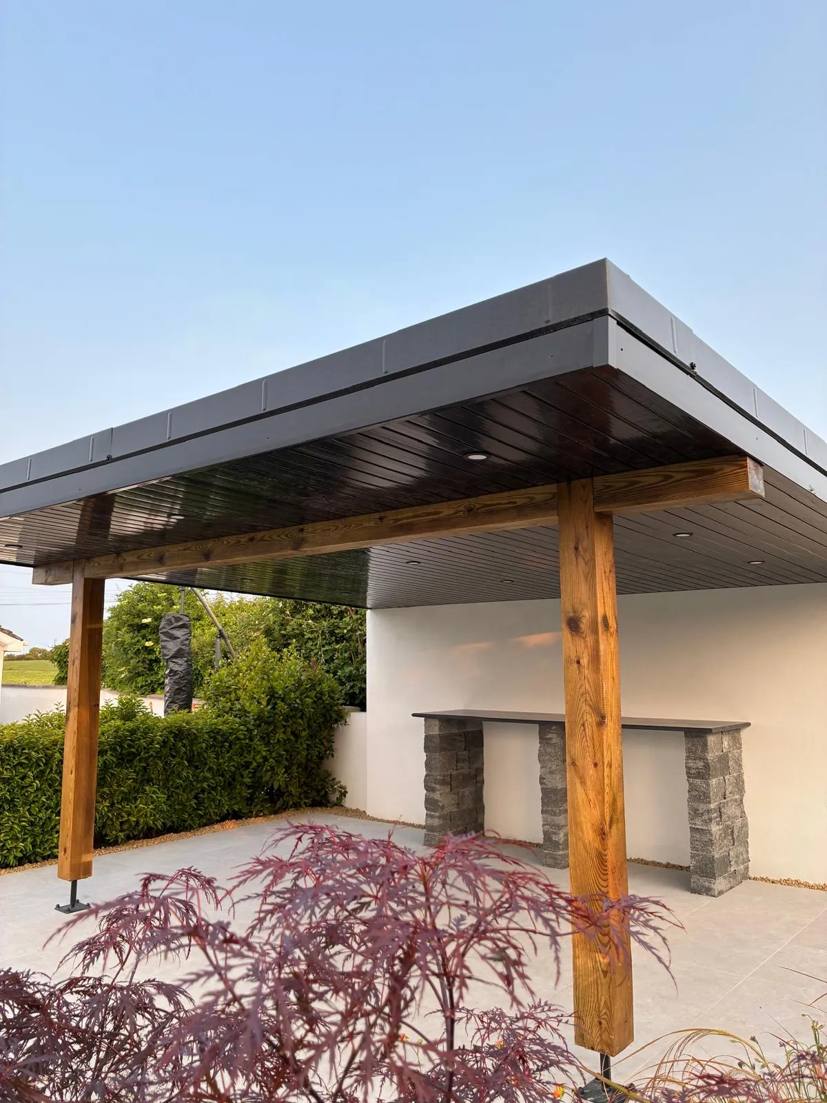 Timber pergola over a paved area with a stone-clad base