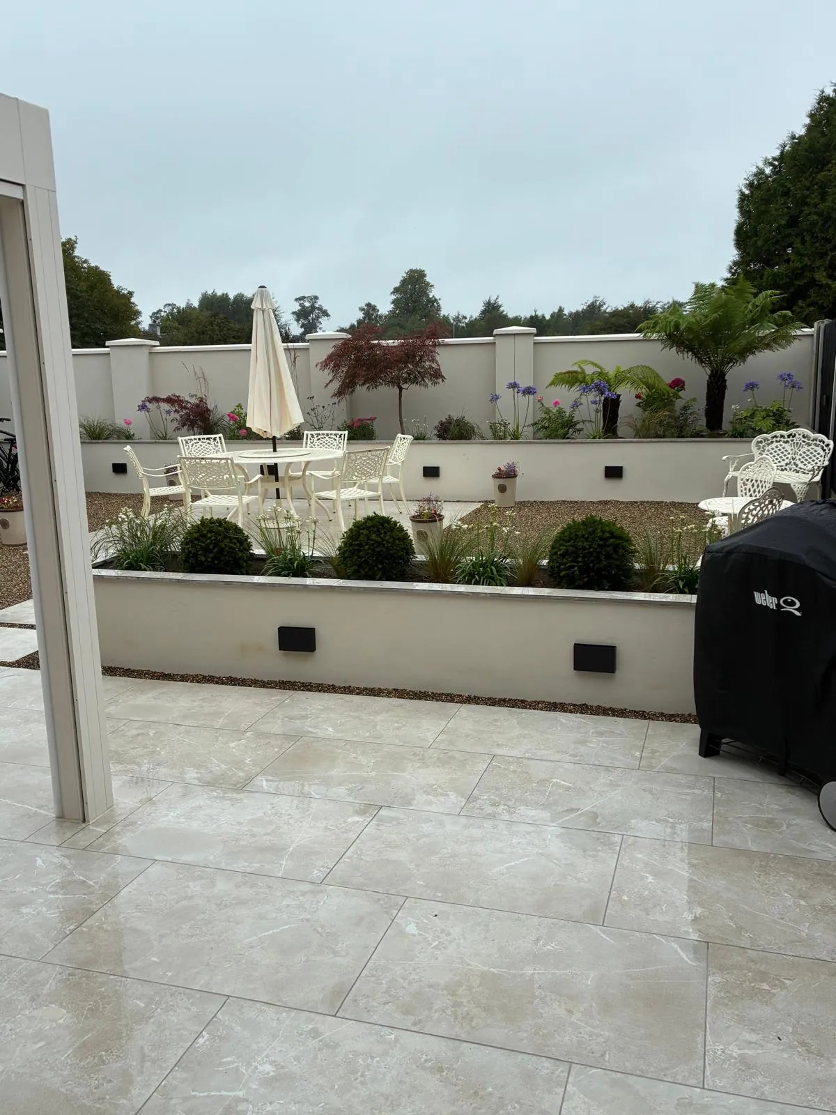 Paved patio with raised stone-clad garden beds, outdoor dining furniture and a barbecue