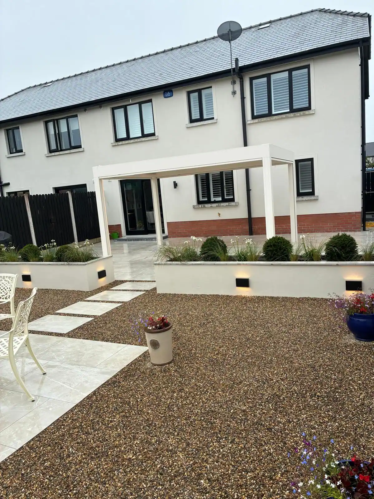 Paved and gravel entrance path with a pergola canopy and raised planters