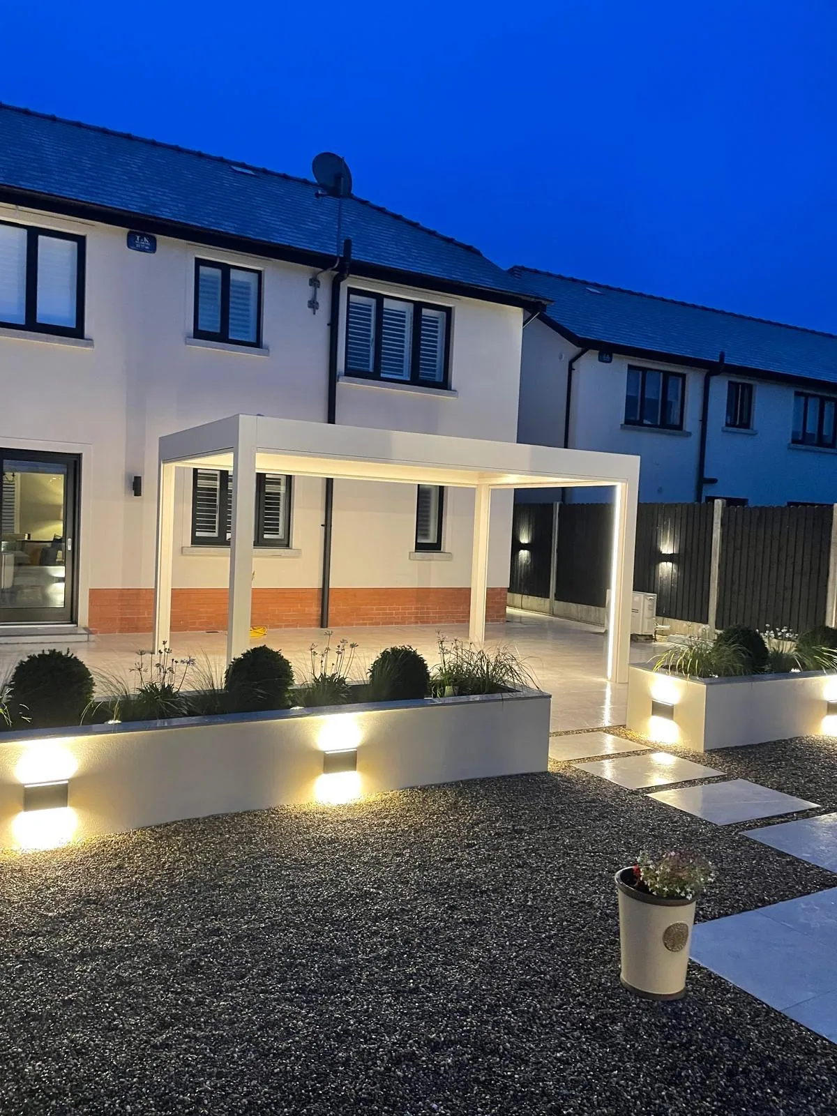 Large pergola over a paved and gravel patio, lit at dusk