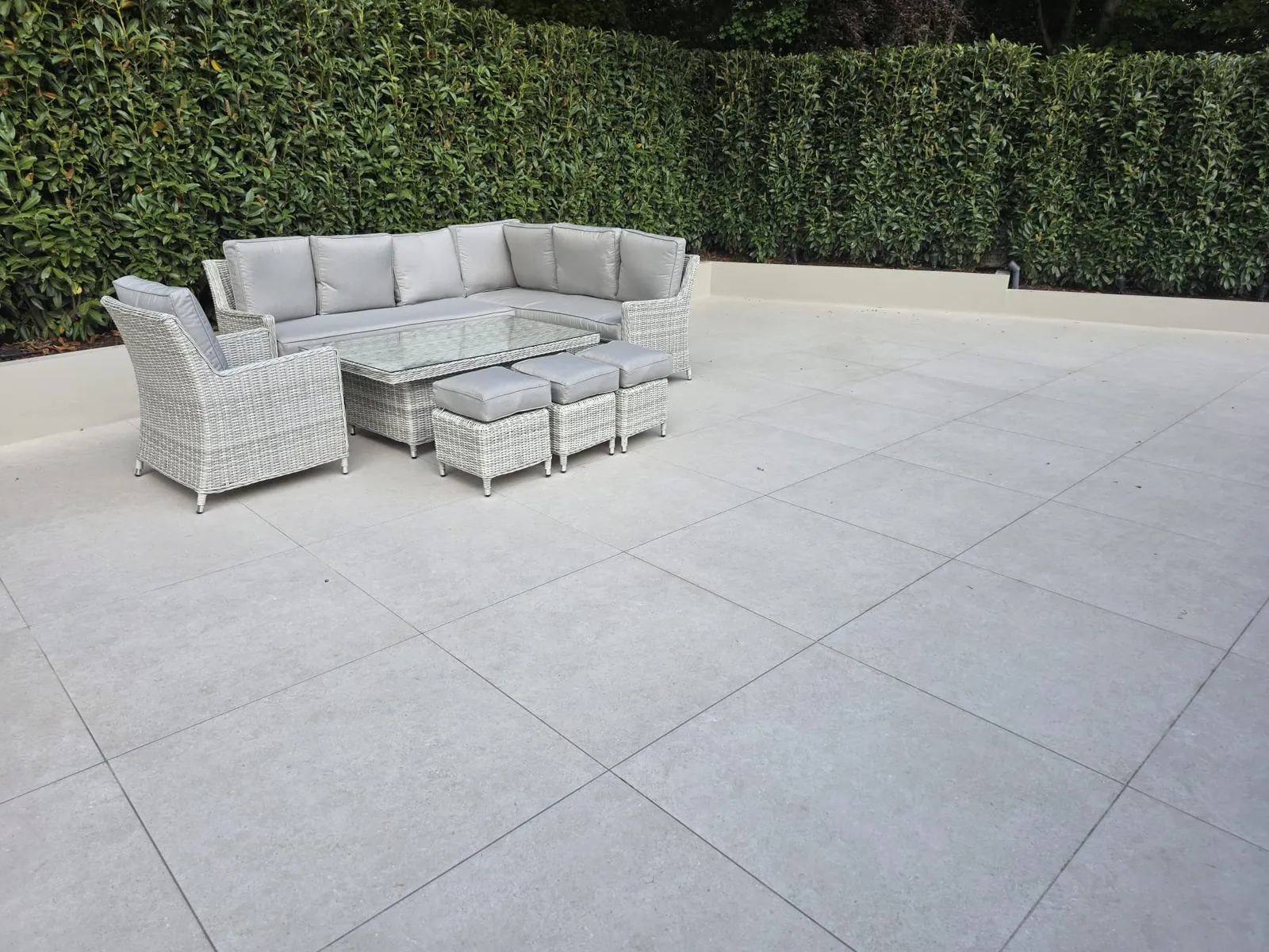 Wide pale patio with an outdoor corner sofa against a hedge