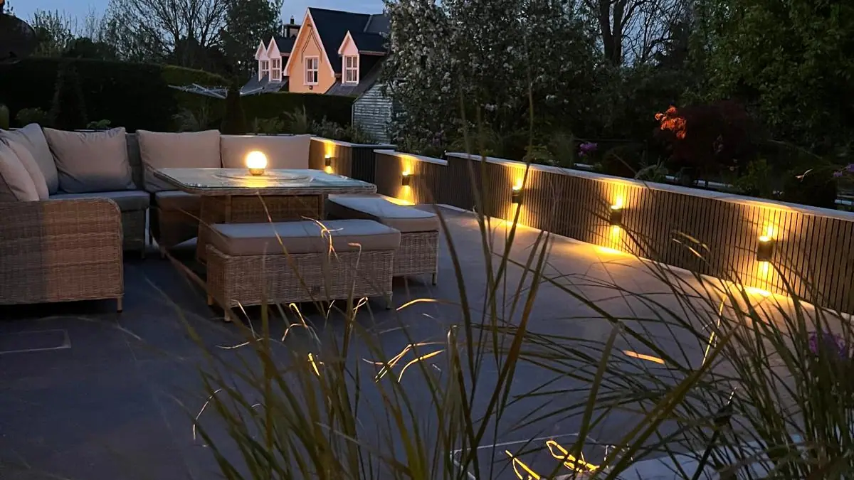 Outdoor lounge seating on a dark paved patio with built-in lighting at dusk